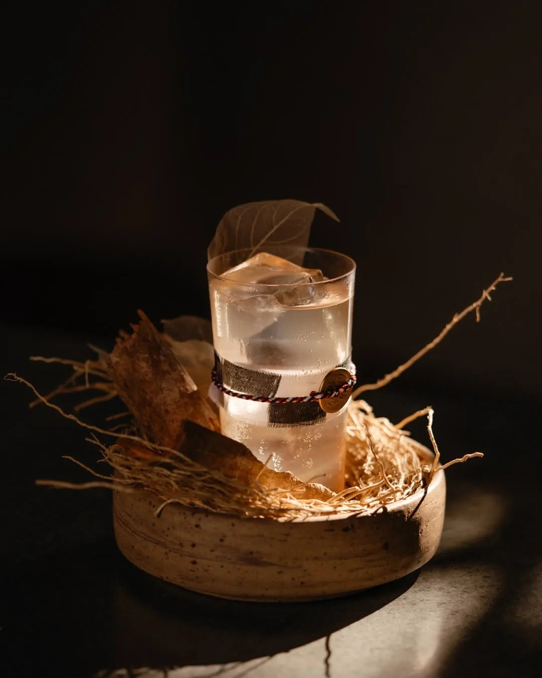 A zero-proof highball in a stoneware bowl of dried roots